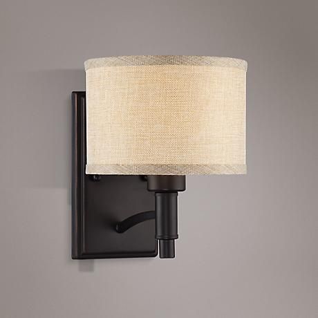 a black wall light with a white shade on the lamp and a gray wall behind it