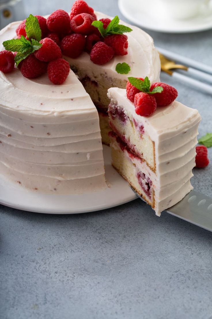 a cake with white frosting and raspberries is cut from the side on a plate