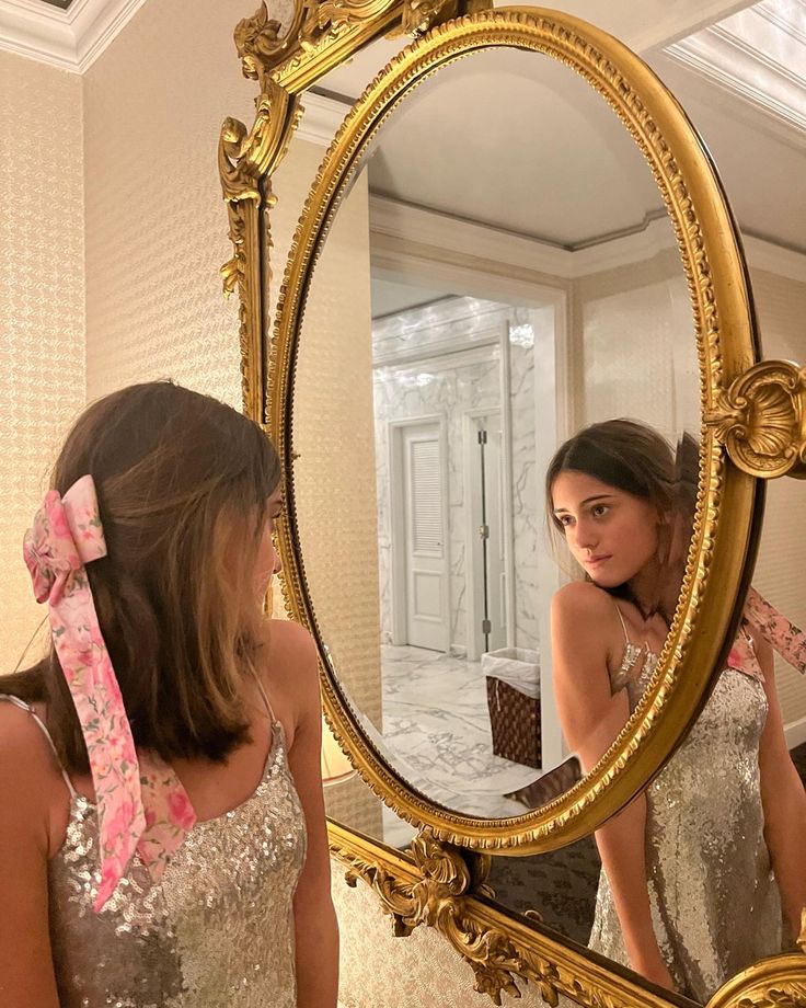 a woman is looking at her reflection in the mirror while wearing a pink and silver dress