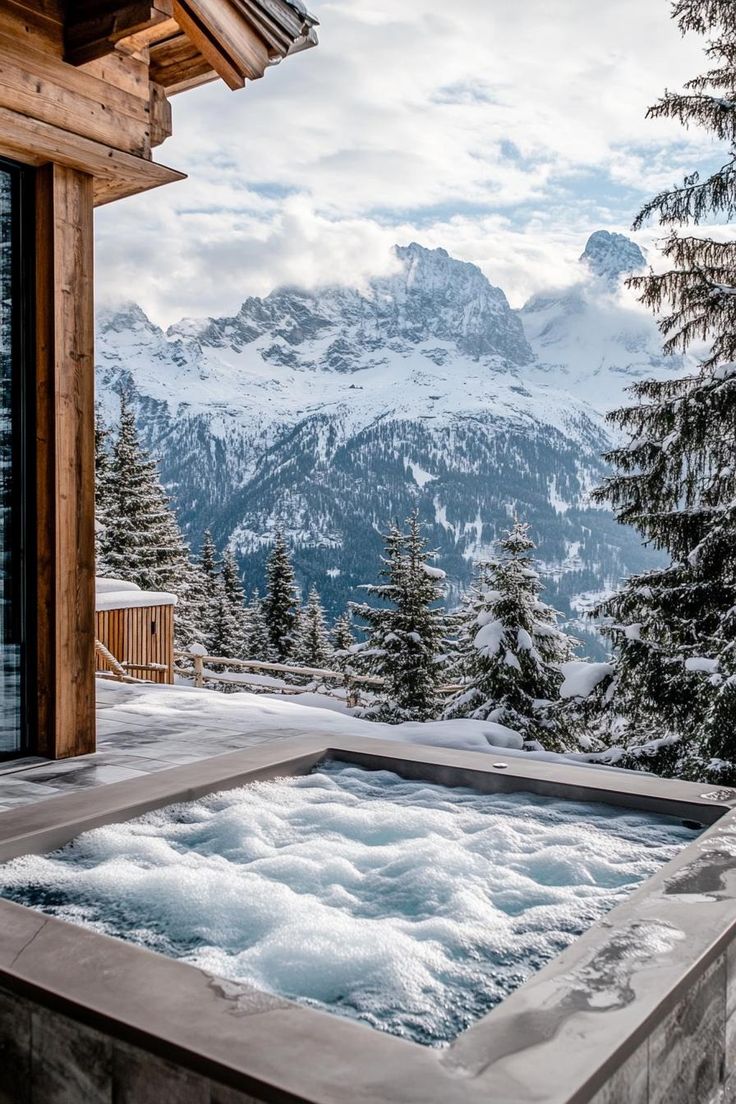 an outdoor hot tub in the snow with mountains in the backgroung and pine trees