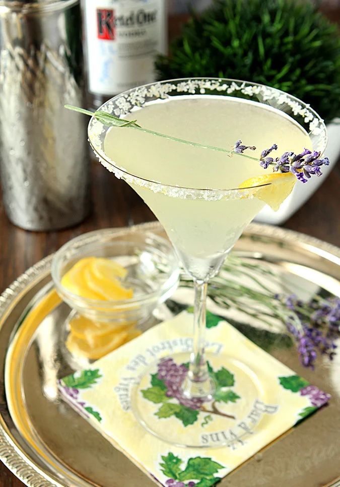 a drink in a martini glass on a silver plate with lavenders and lemon wedges