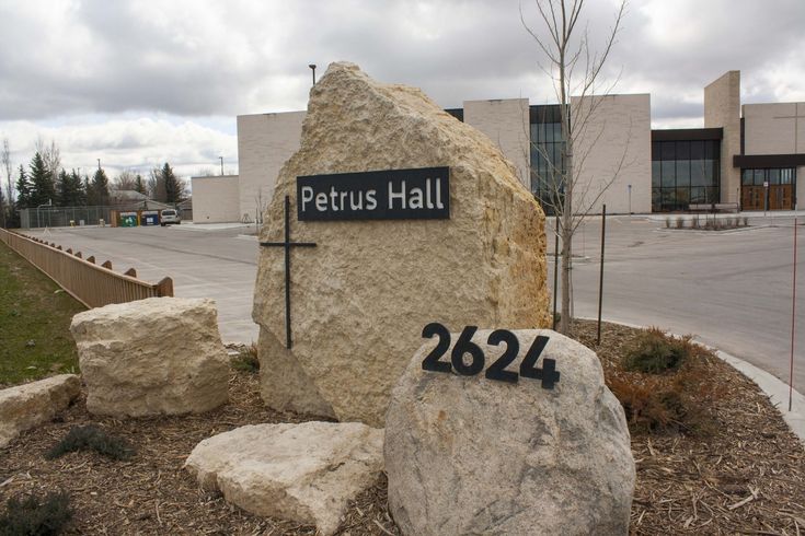 a large rock sitting in front of a building next to a sign that says petrus hall