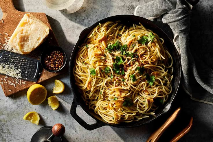 a skillet filled with pasta and garnished with parsley next to sliced lemons