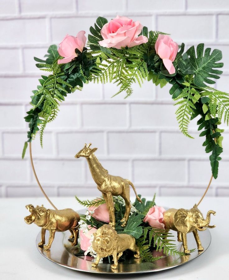 a metal tray with pink roses and gold figurines on it, surrounded by greenery