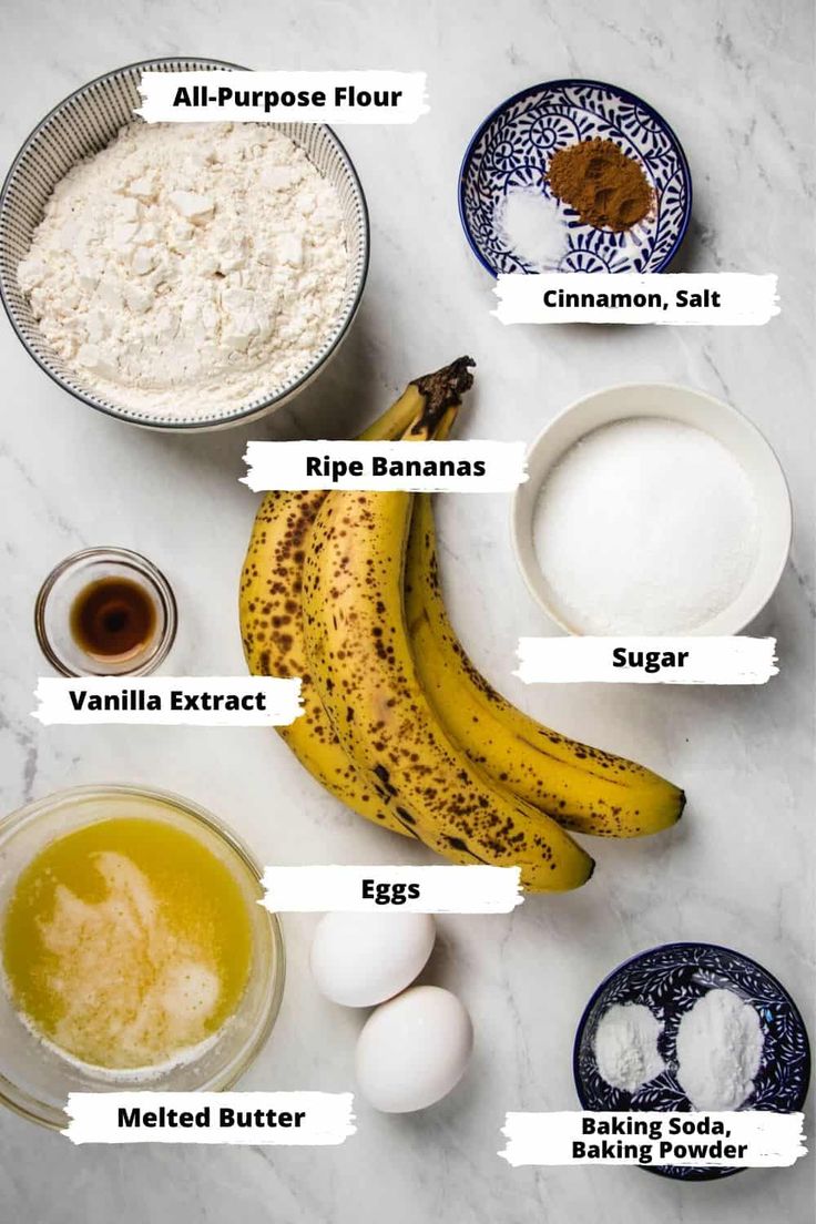 ingredients to make banana bread laid out on a white counter top, including bananas, eggs, flour, cinnamon and sugar