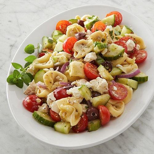 a white plate filled with pasta salad on top of a marble countertop next to a fork