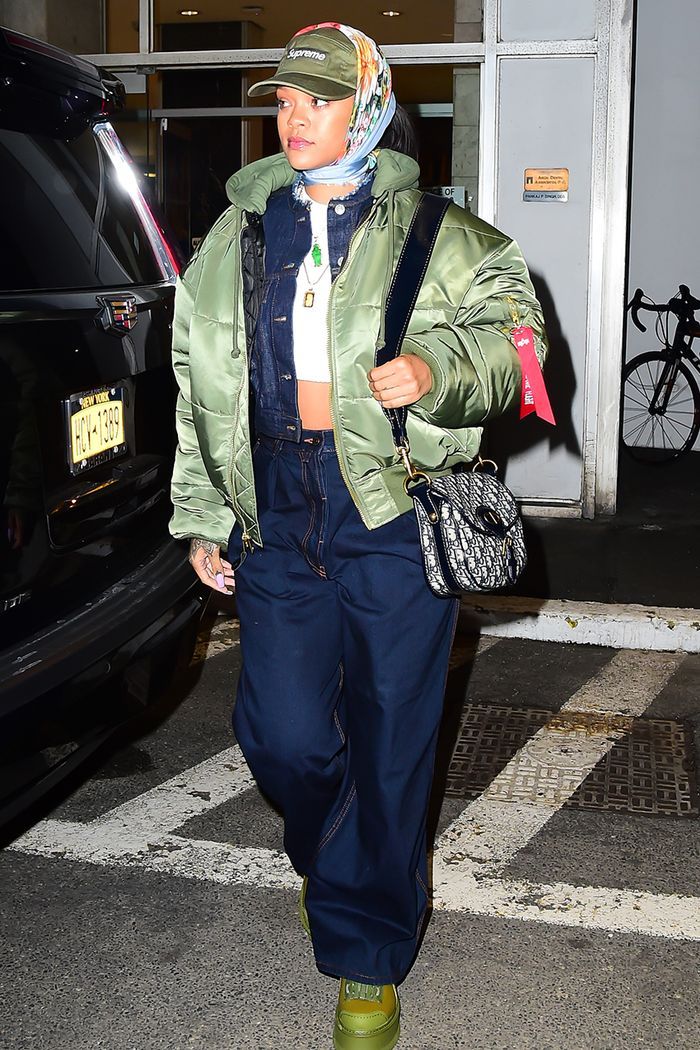 a woman in green jacket and blue pants walking down the street with her hand on her hip