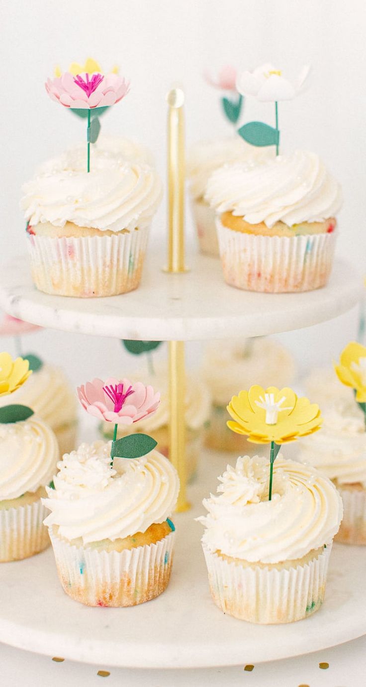 cupcakes with white frosting and yellow flowers on top are sitting on a three - tiered cake stand