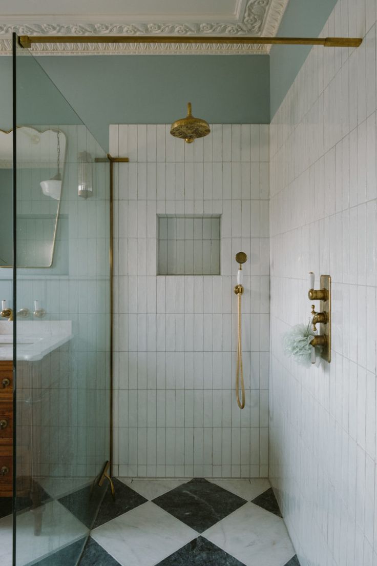 a walk in shower sitting next to a white sink and tiled floor with gold faucet