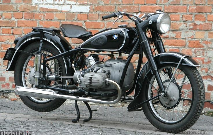 an old black motorcycle parked next to a brick wall