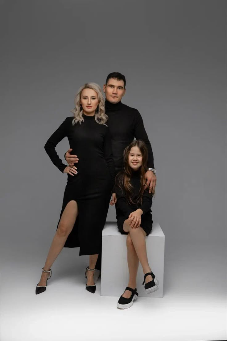 two adults and a child posing for a photo in front of a gray background with the caption's name on it