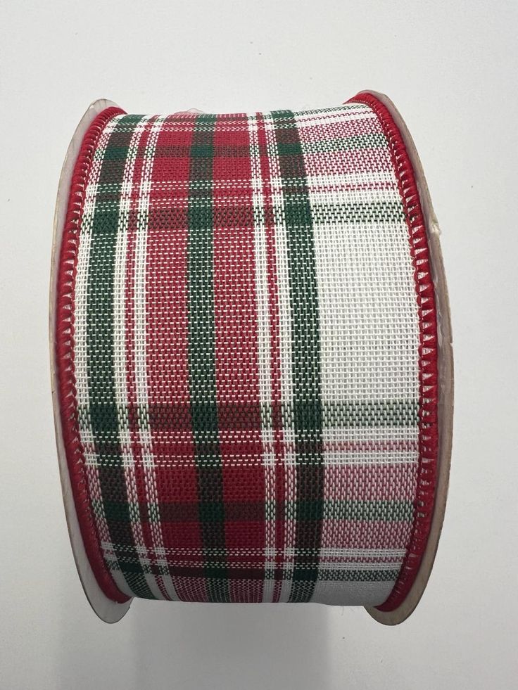 a spool of red and green plaid ribbon on a white surface with a black edge