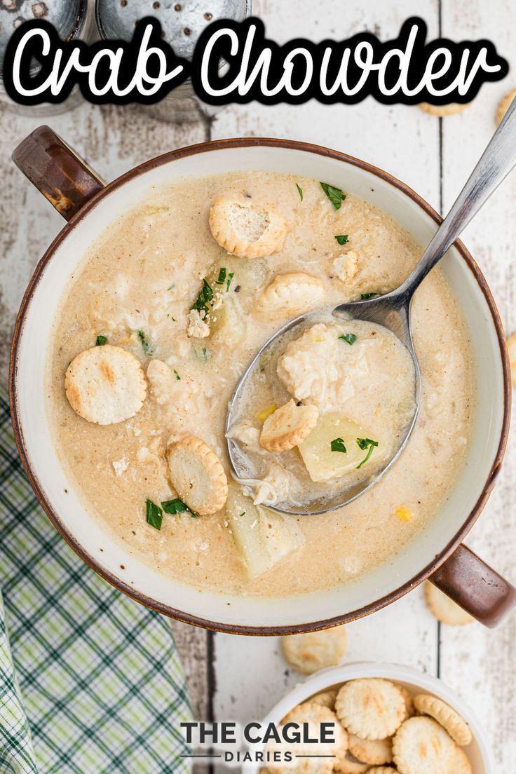 a bowl of crab chowder next to two bowls of crackers and spoons