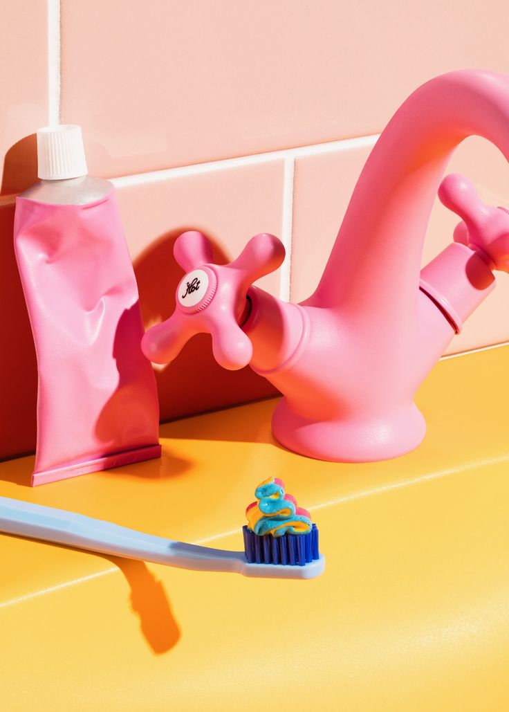 a pink toothbrush sitting on top of a yellow counter next to a cupcake