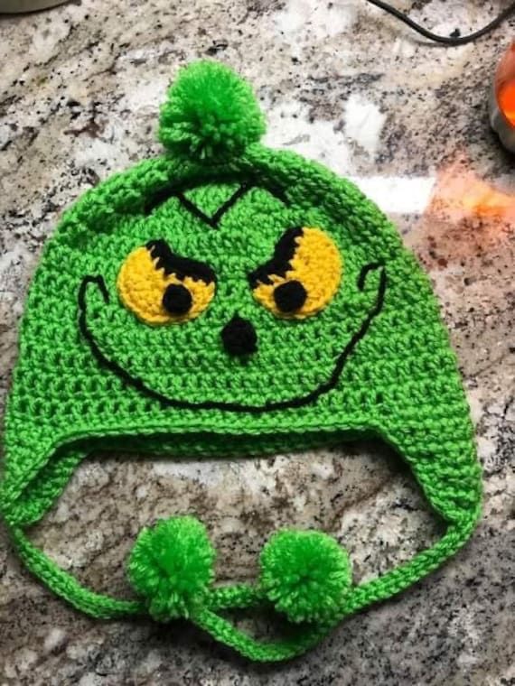 a crocheted green hat with yellow eyes and a pom - pom