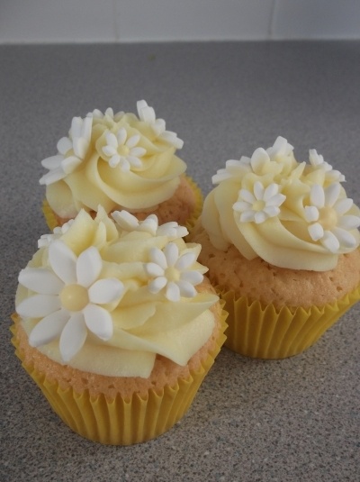 three cupcakes with white frosting and flowers on them sitting on a counter