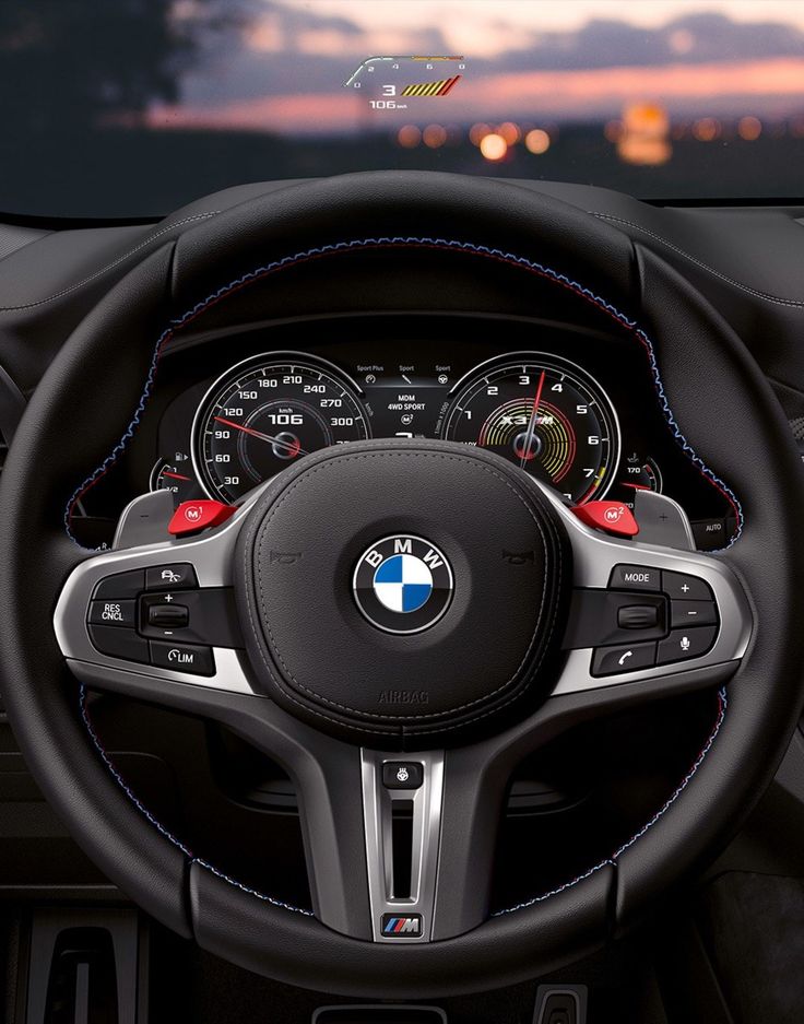 the steering wheel and dashboard of a bmw car with city lights in the back ground