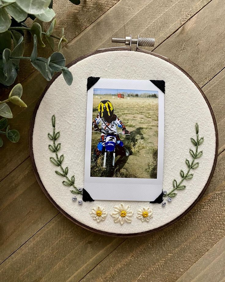 an embroidered photo frame with flowers around it and a motorcyclist in the background