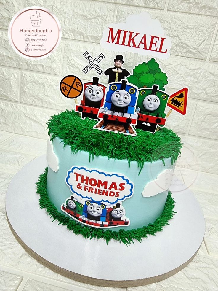 there is a thomas the train cake with grass on it's top and decorations