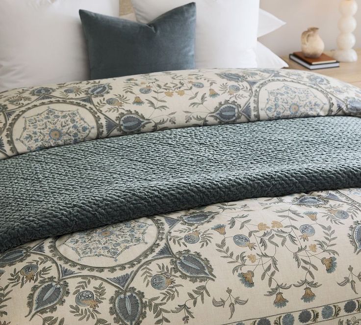 a bed with blue and white comforters on top of it next to a night stand