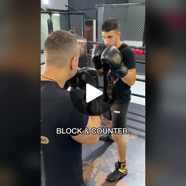 the man is practicing his boxing skills in the gym with another man who is looking on