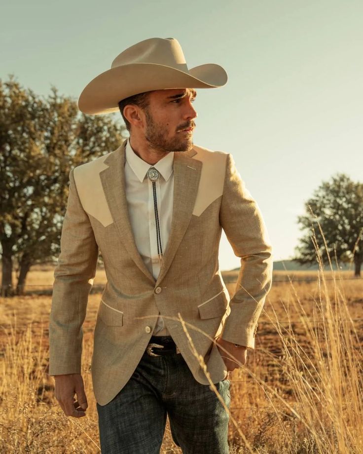 a man in a suit and cowboy hat standing in the middle of an open field