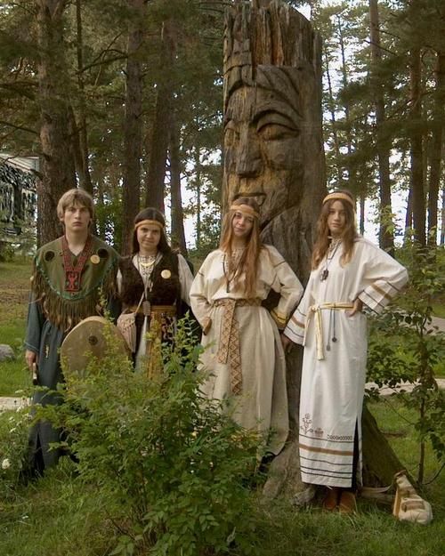 four people standing in front of a carved totem with trees and grass behind them