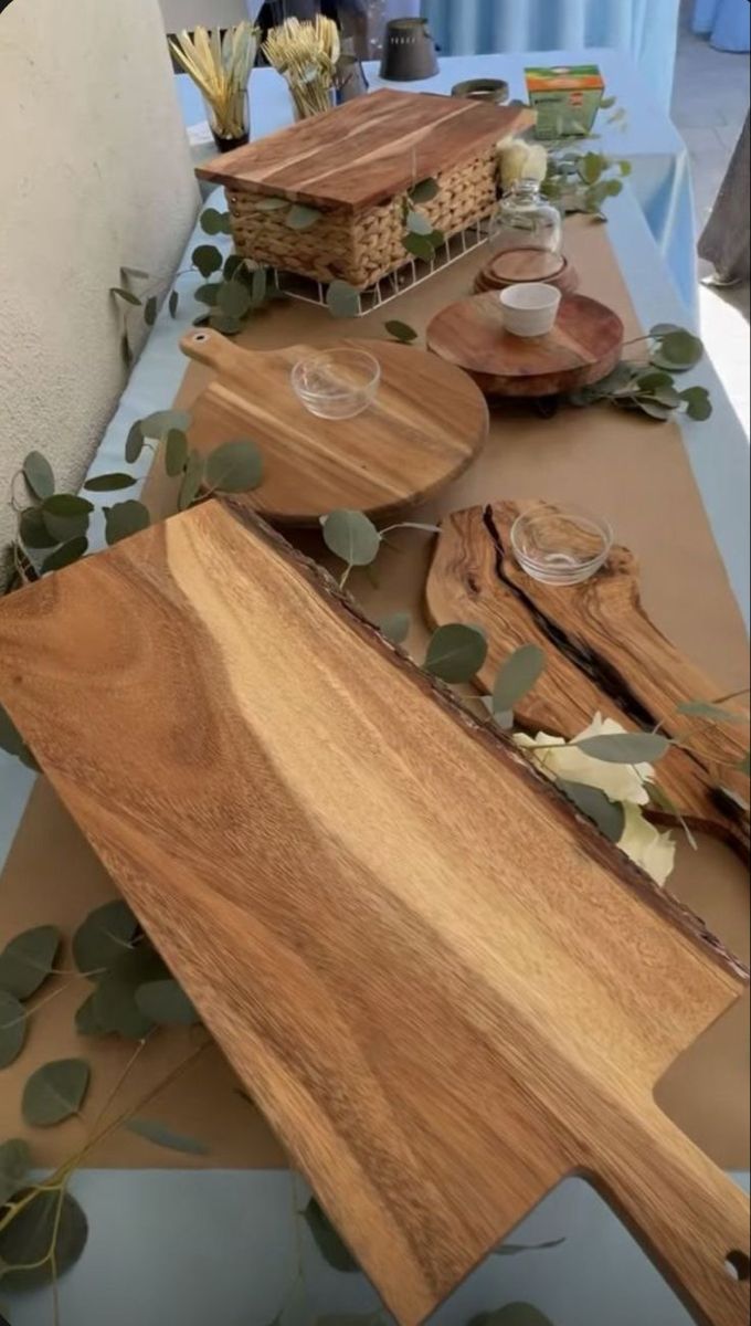 the table is set with wooden cutting boards and plates on it, along with greenery