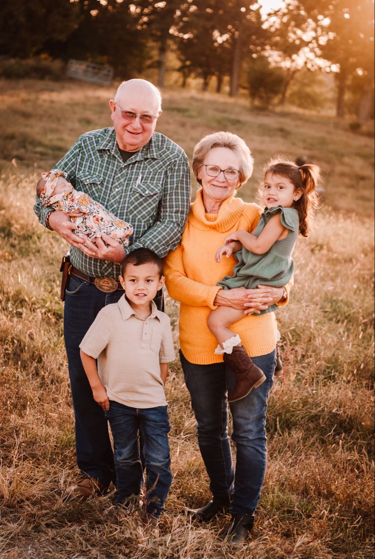 an older man, woman and two children posing for a photo in a field at sunset