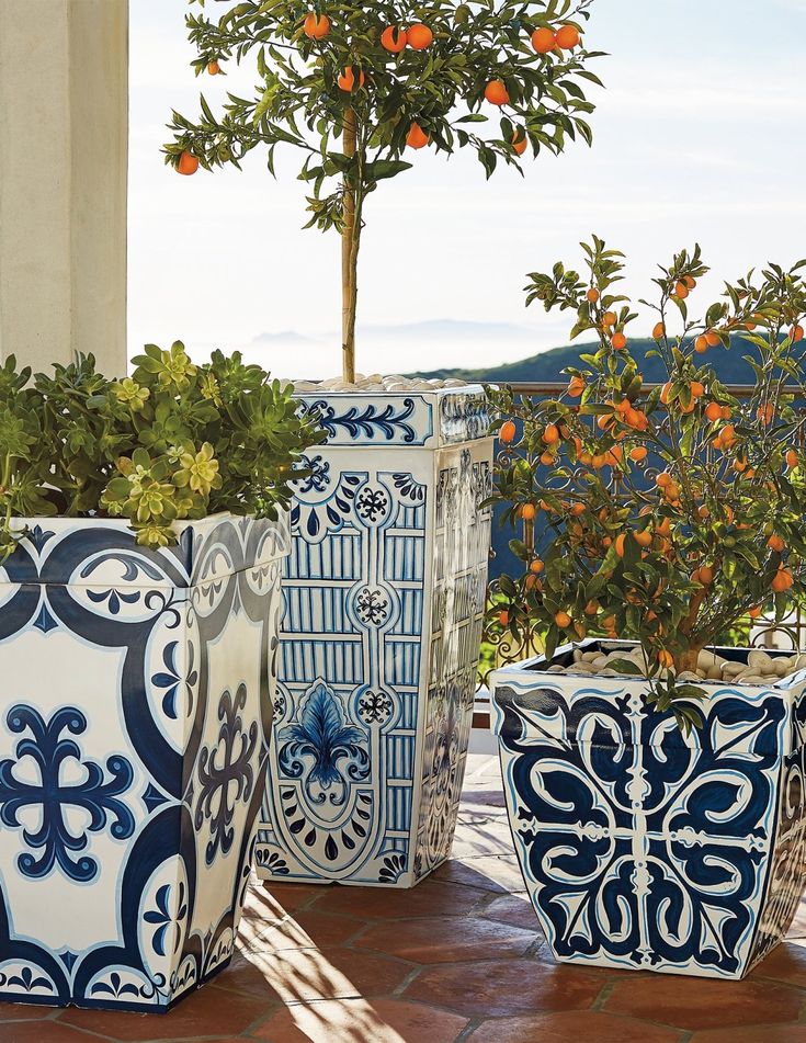 four blue and white vases sitting on top of a tiled floor next to an orange tree