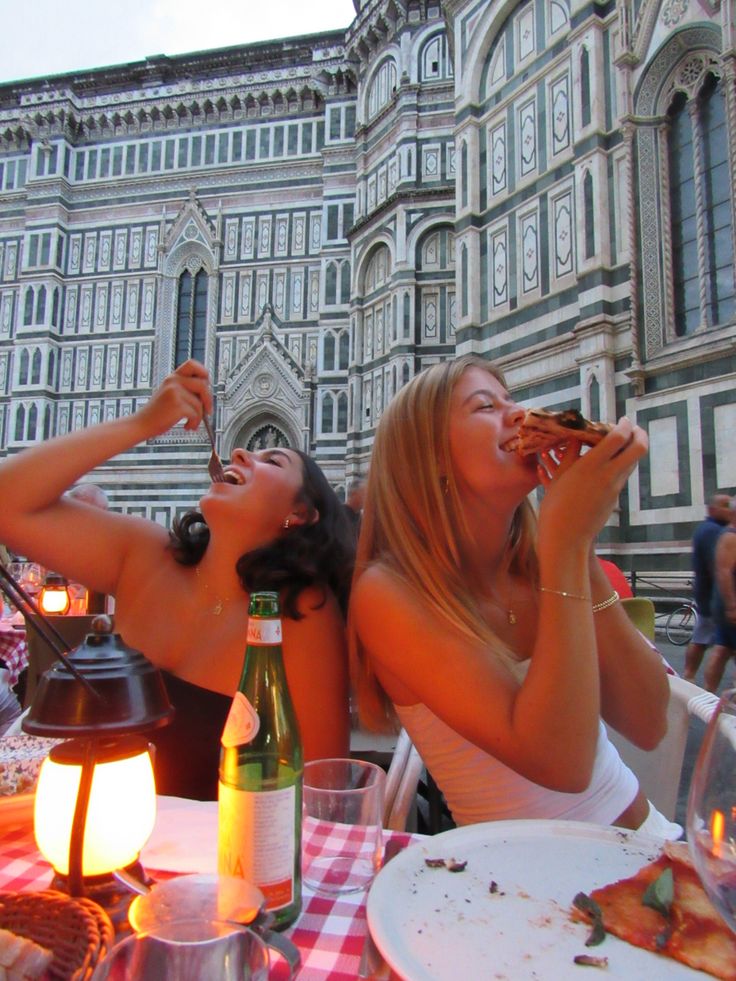 two beautiful women sitting at a table eating pizza