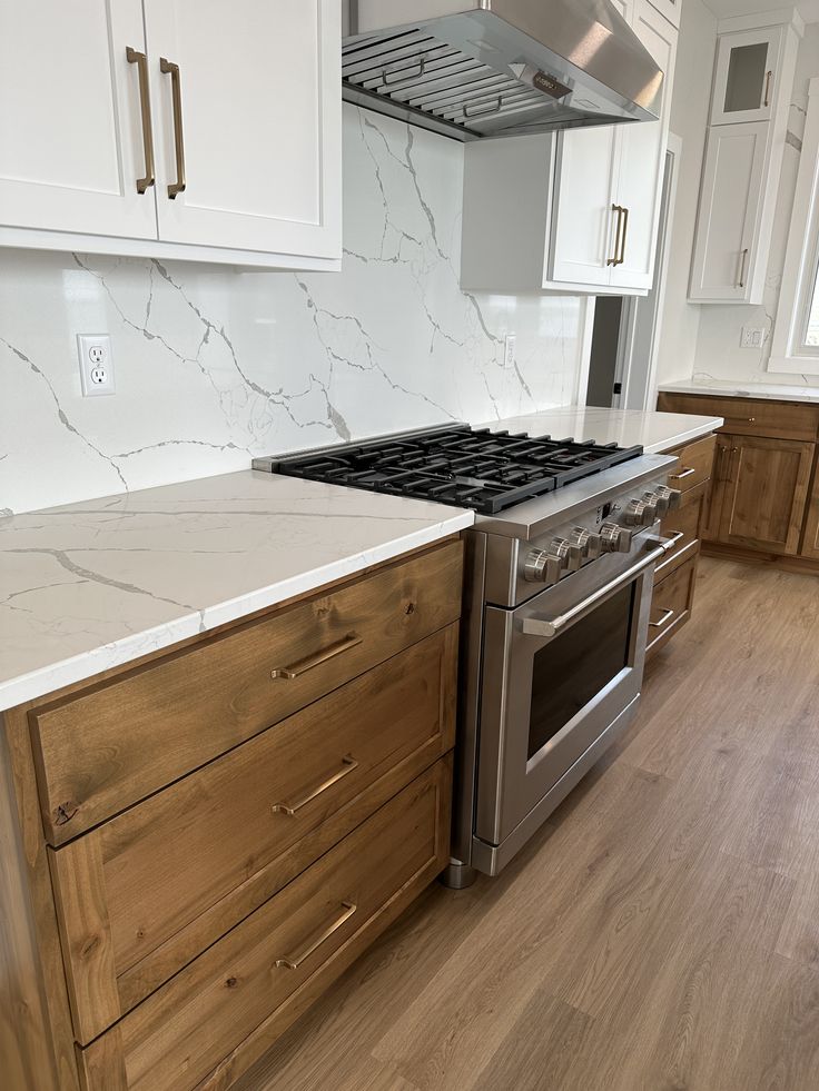 a stove top oven sitting inside of a kitchen next to white cabinets and drawers on a wooden floor