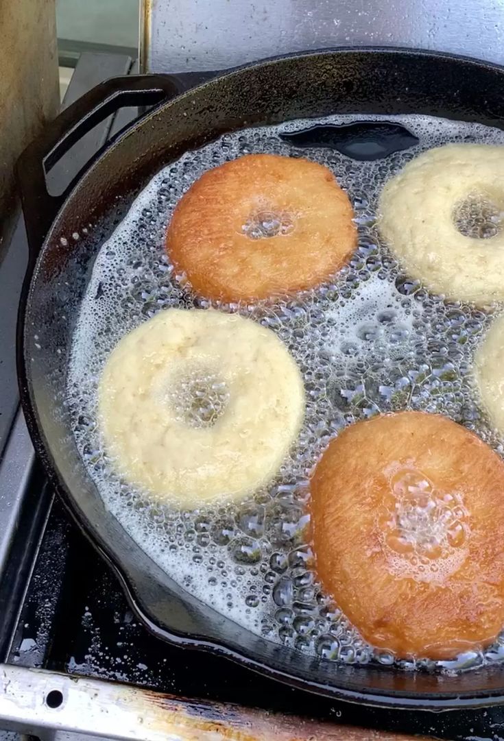 three donuts frying in oil on top of an open skillet with water