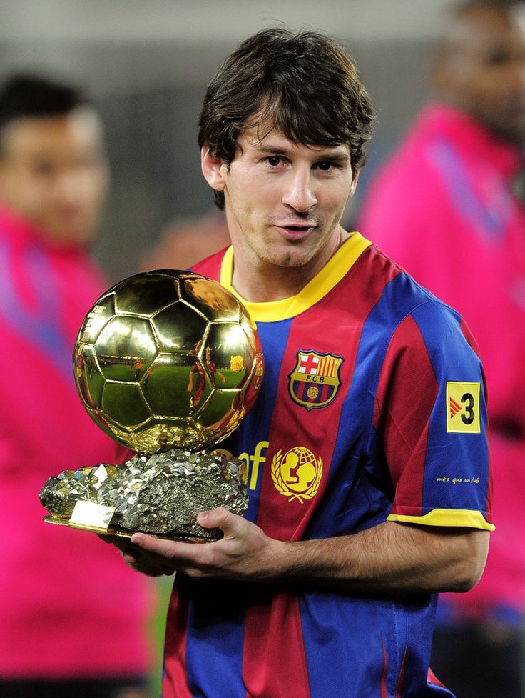 a man holding a soccer ball and trophy in his hands while wearing a red, blue and yellow shirt