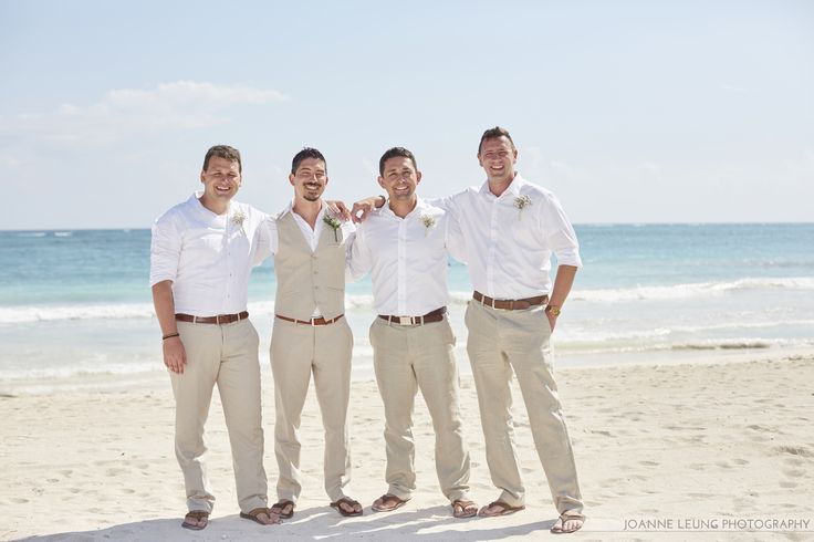 three men in white shirts and tan pants standing on the beach with their arms around each other