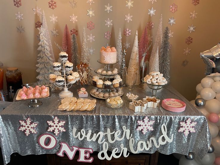 a table topped with lots of desserts next to balloons and snowflakes on the wall