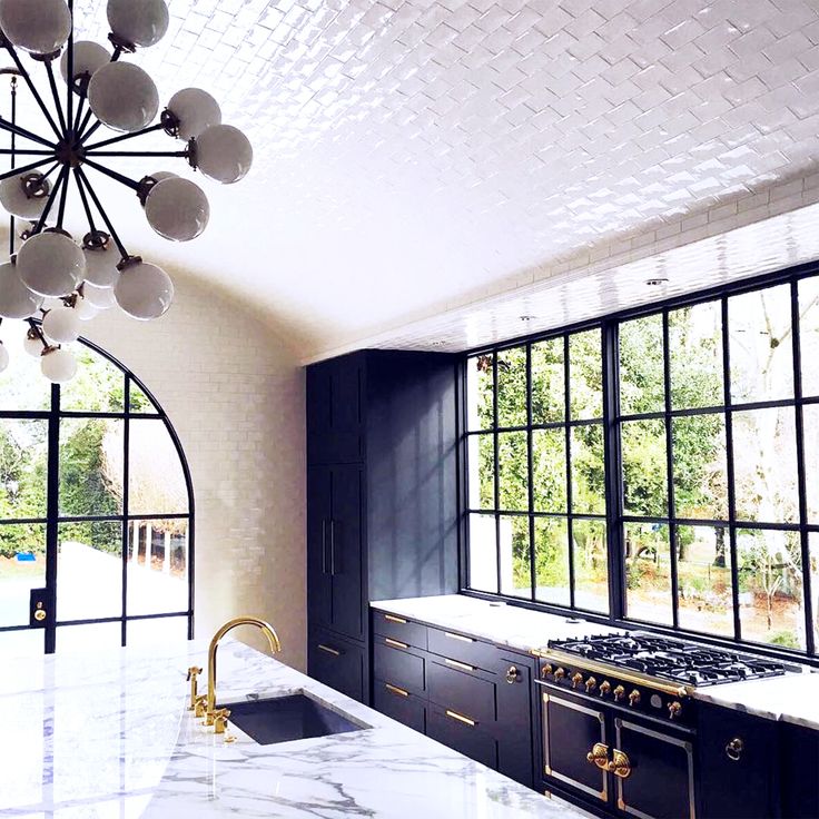 a large kitchen with marble counter tops and black cabinetry, along with a chandelier hanging from the ceiling