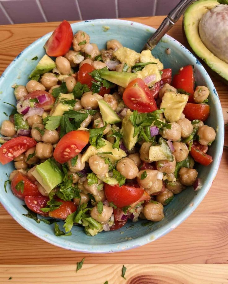 a salad with chickpeas, tomatoes and avocado in a blue bowl