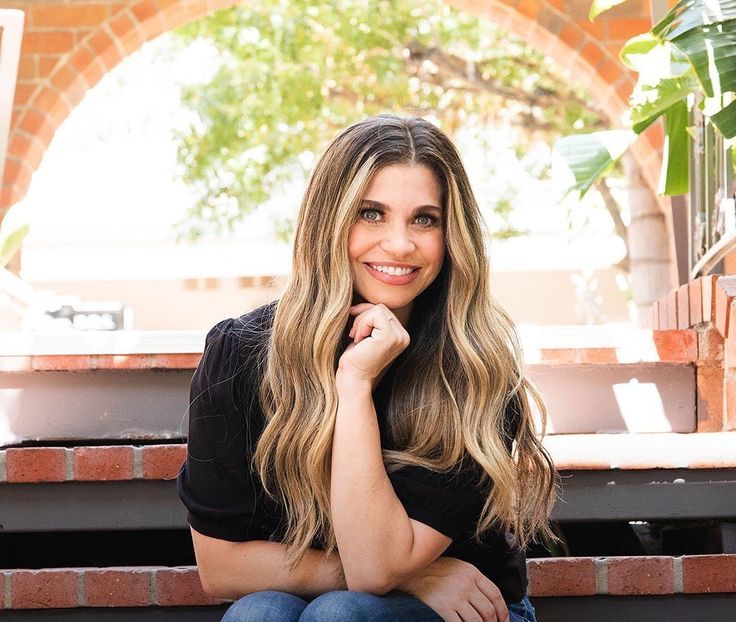 a beautiful woman sitting on top of a bench next to a brick wall and potted plant