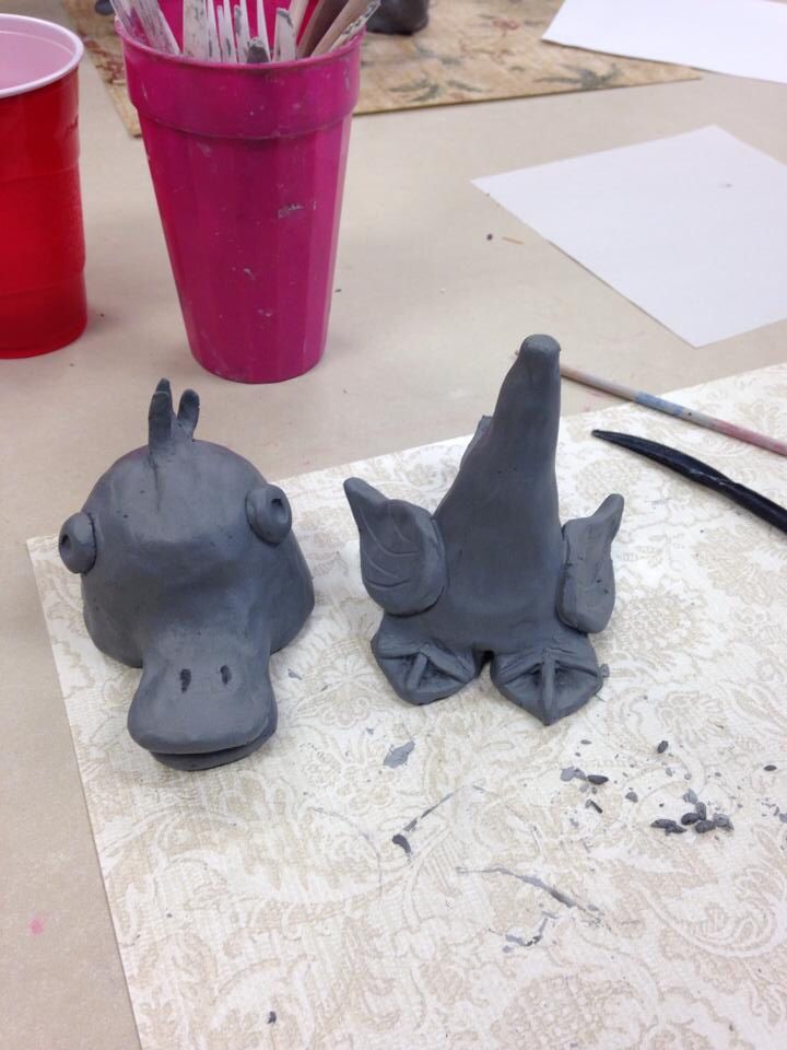 two clay animals sitting on top of a table next to paintbrushes and paper