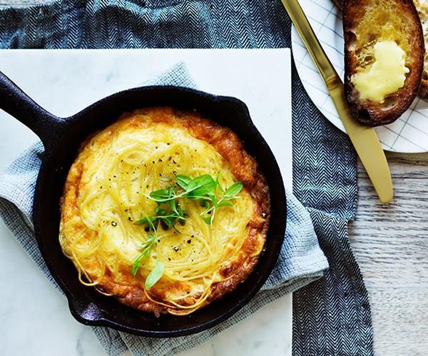 a skillet filled with spaghetti and cheese on top of a table next to bread