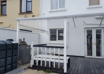 a white house with a wooden deck and black trash can in front of the door