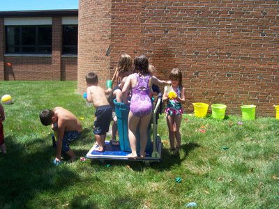 several children are playing in the grass near a brick building with buckets on it