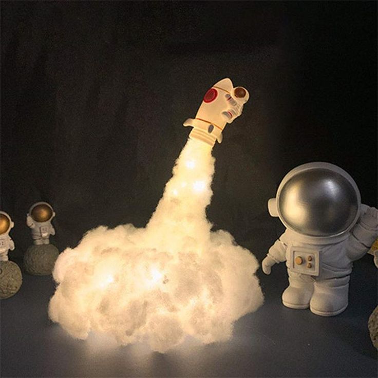 an astronaut rocket launching into the sky with other small toy figures around it on a black background