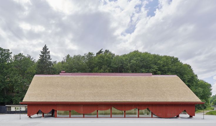 a large red barn sitting in the middle of a parking lot next to a forest