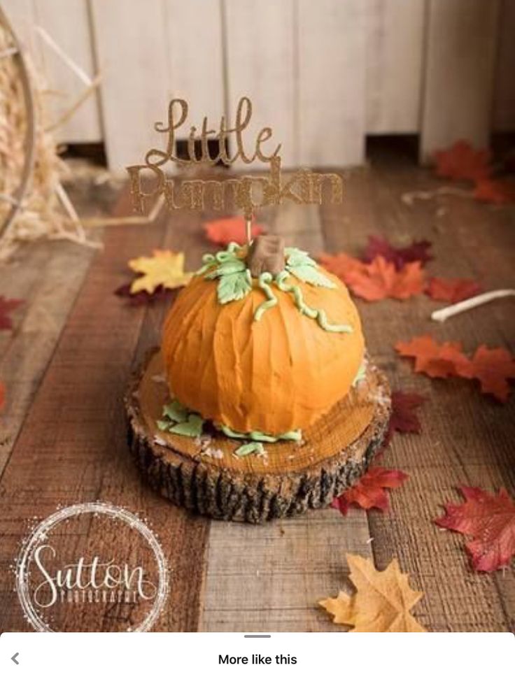 a pumpkin cake sitting on top of a wooden table next to fall leaves and a sign that says little pumpkin