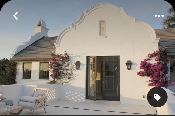 a white house with pink flowers on the front and side windows, next to a patio