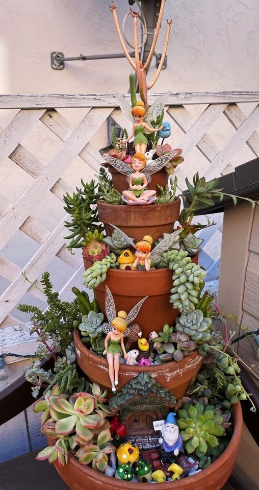 a very tall potted planter filled with lots of succulents and little fairy figurines