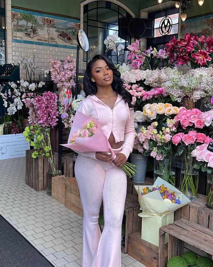 a woman standing in front of flower shop with flowers on display behind her and holding a bouquet