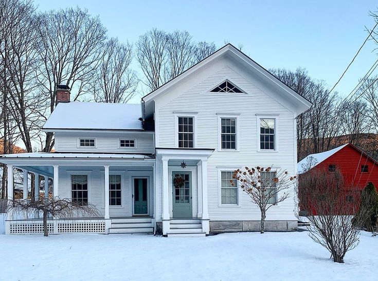 a white house in the middle of winter with snow on the ground and trees around it